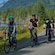 A family riding bicycles along a river with Mendenhall Glacier in the distance